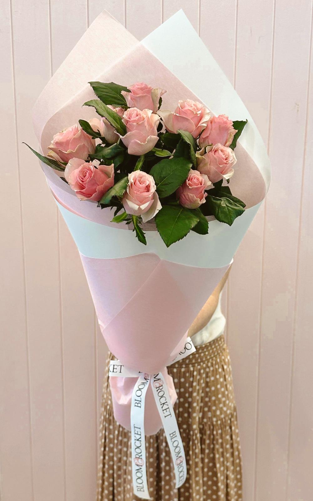 A bouquet of blush pink roses wrapped in white and pink paper with a ribbon. Bloom and Rocket Florist, Taringa. Brisbane Flower delivery.