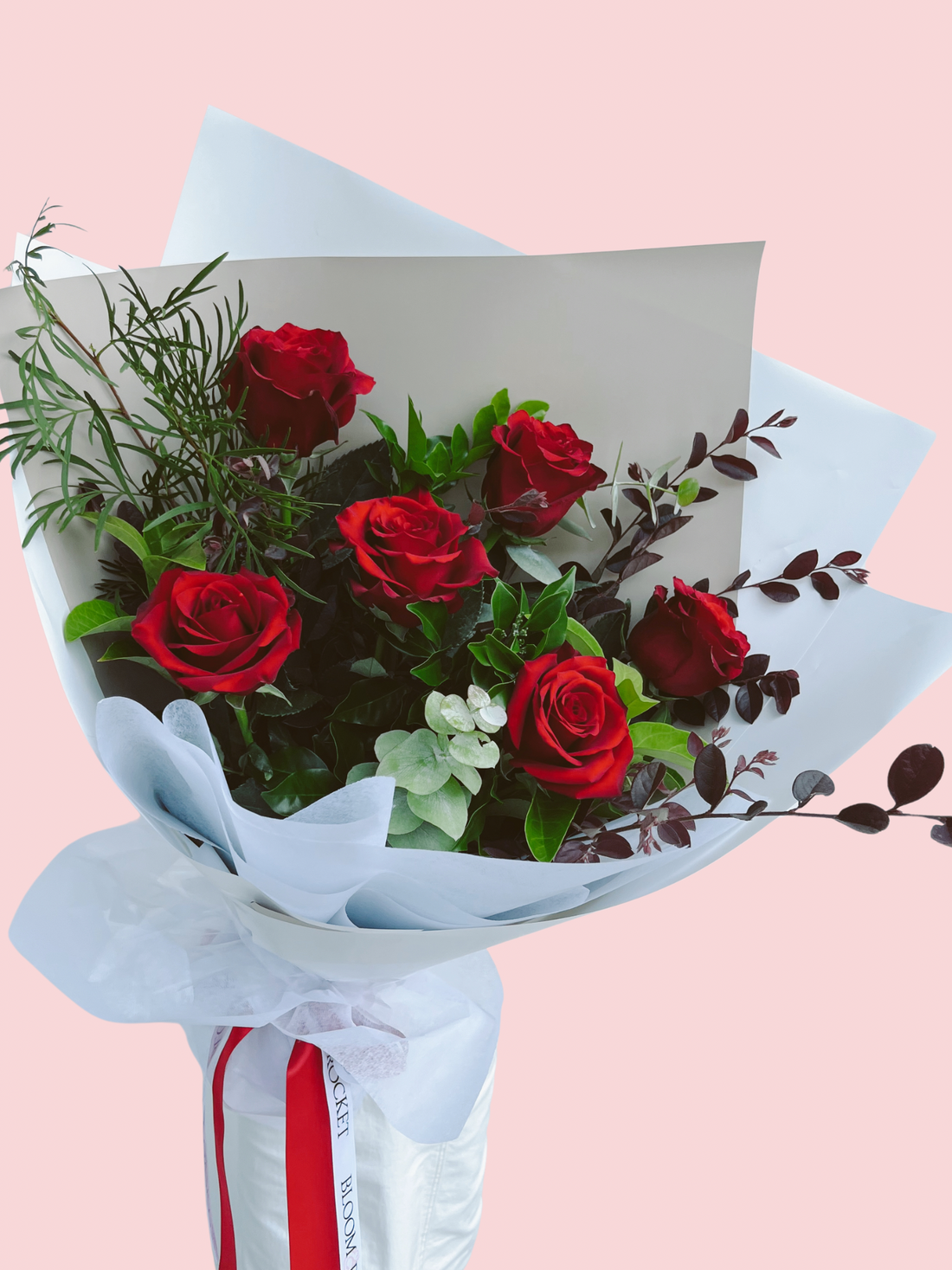 A bouquet of red long stem roses with foliage, wrapped with white paper and a red and white ribbon. Half Dozen red roses. Brisbane Flower delivery. Bloom and Rocket Florist.