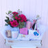 A gift basket containing an assortment of items including chocolates, a bottle of Chandon Sparkling Wine, eye masks, bath soap, body butter, and a candle, all arranged in a white box with a pink background. Brisbane gift delivery. Bloom and Rocket Florist.