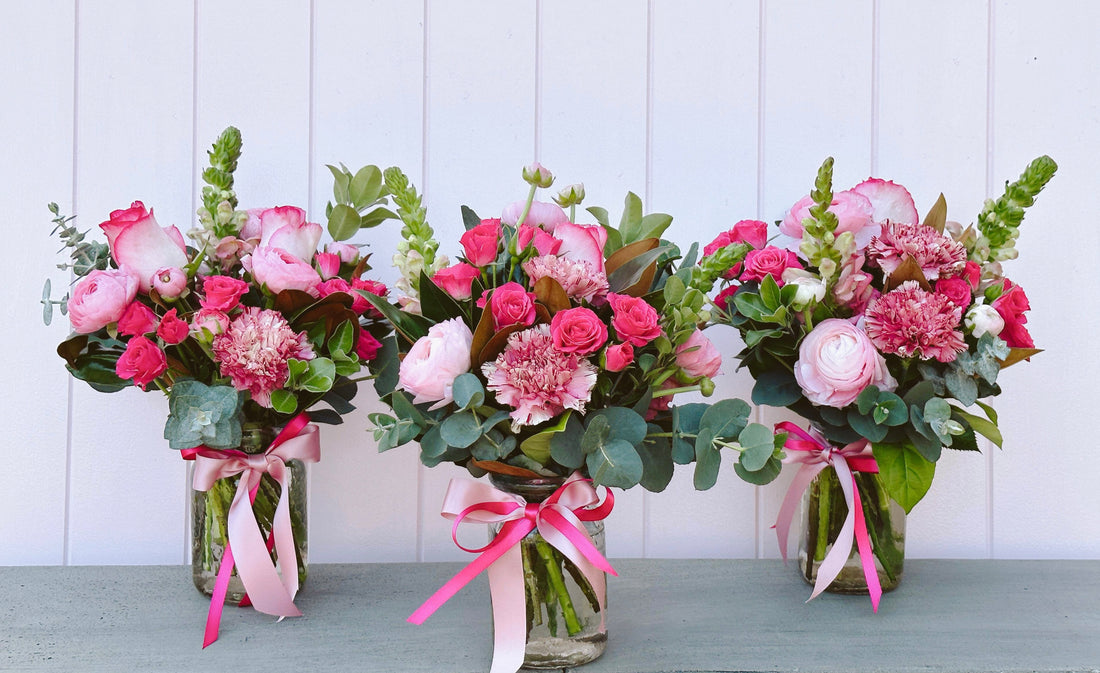 Three floral arrangements with pink and green flowers, tied with ribbons, placed in clear vases.